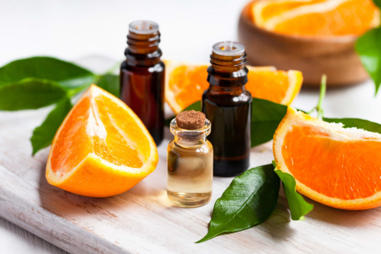 Concept of natural organic orange essential oil for skin face and body health care. Moisturizing, aromatherapy, detox treatment, anti-stress effect. Fresh fruit, green leaves, white background