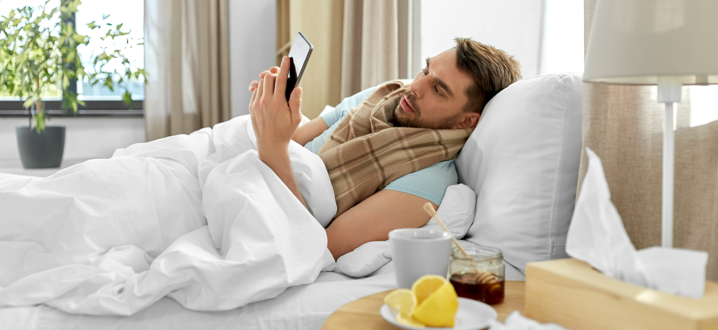 health, illness and people concept - sick man with smartphone in bed at home