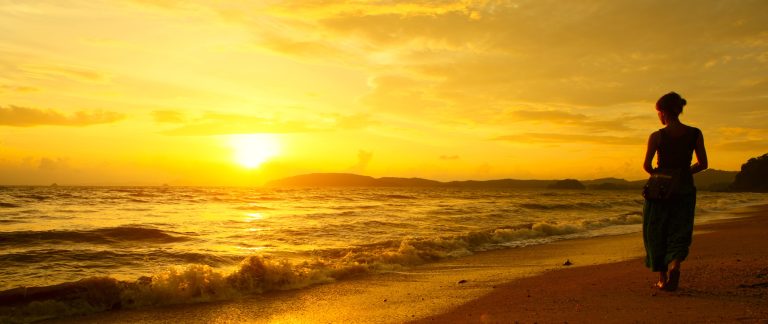 Young woman walking on beach under sunset light
